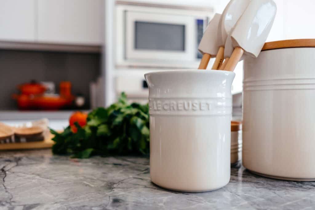 Un pot blanc avec des cuillères et des ustensiles sur un comptoir.